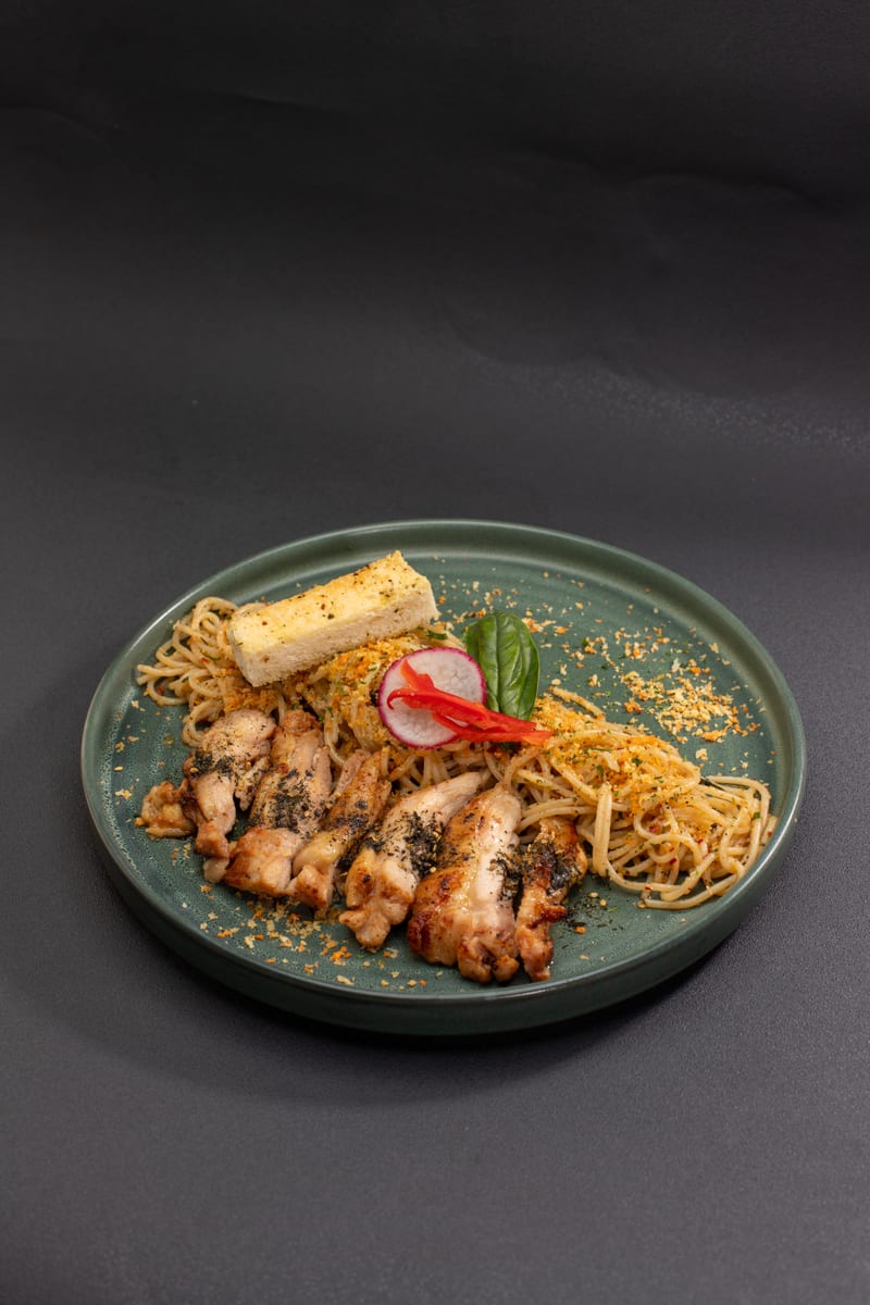 Plate of aglio olio pasta topped with sliced grilled chicken