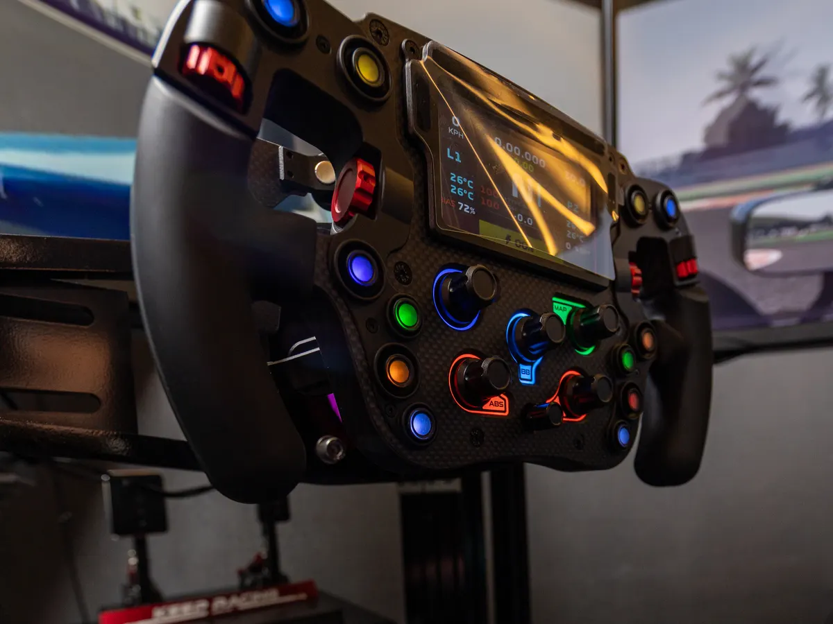 A direct-drive steering wheel at Race.inc, its buttons lit in the dark